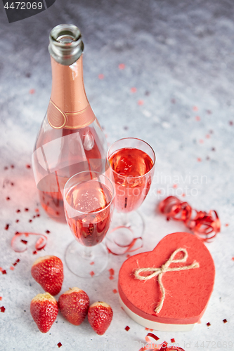 Image of Bottle of rose champagne, glasses with fresh strawberries and heart shaped gift