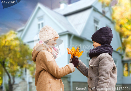 Image of kids with autumn maple leaves over house outdoors