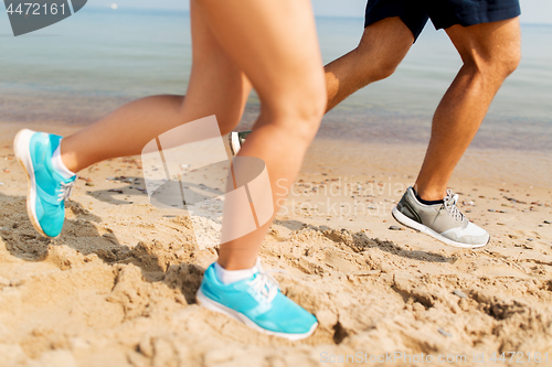 Image of legs of sportsmen in sneakers running along beach