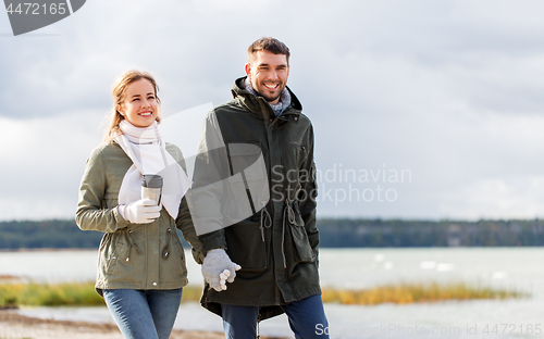 Image of couple with tumbler walking along autumn beach