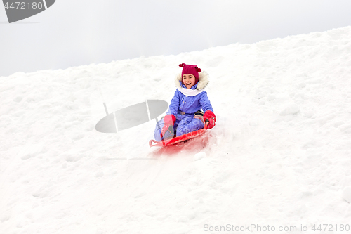 Image of girl sliding down on snow saucer sled in winter