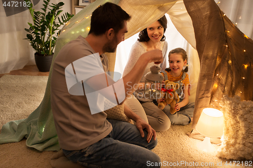 Image of happy family playing in kids tent at night at home