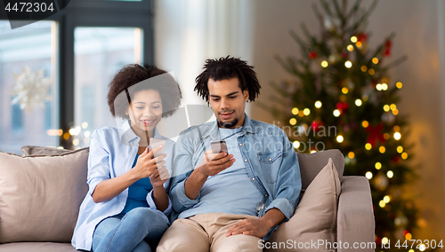 Image of happy couple with smartphones at home on christmas