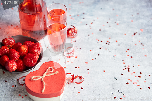 Image of Bottle of rose champagne, glasses with fresh strawberries and heart shaped gift