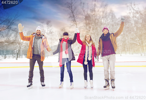 Image of happy friends waving hands on skating rink