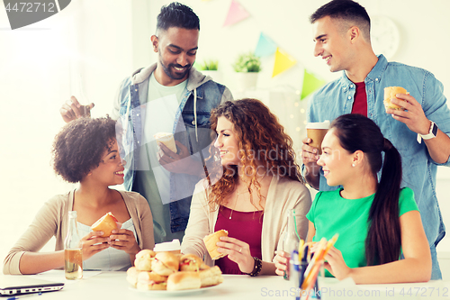 Image of happy friends or team eating at office party