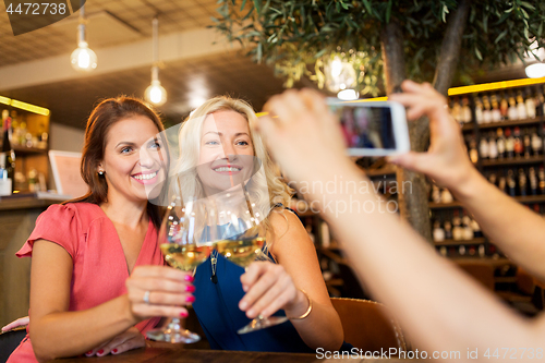 Image of woman picturing friends by smartphone at wine bar