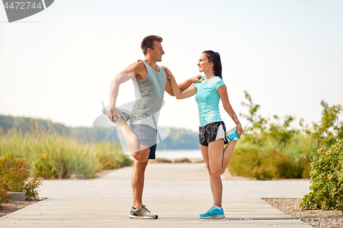 Image of smiling couple stretching legs on beach