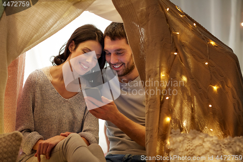 Image of happy couple with smartphone in kids tent at home