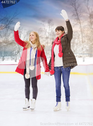 Image of happy female friends waving hands on skating rink