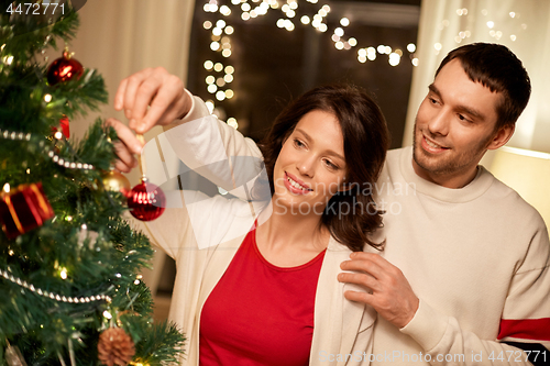 Image of happy couple decorating christmas tree at home