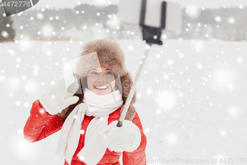 Image of happy woman with selfie stick outdoors in winter