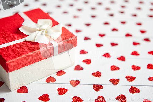 Image of Boxed gift placed on heart shaped red sequins on white wooden table