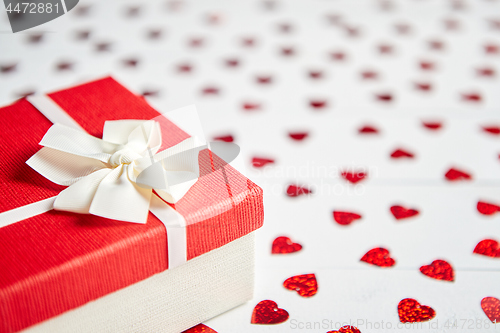 Image of Boxed gift placed on heart shaped red sequins on white wooden table