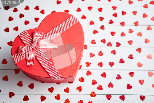 Image of Boxed gift placed on heart shaped red sequins on white wooden table