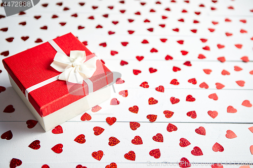 Image of Boxed gift placed on heart shaped red sequins on white wooden table