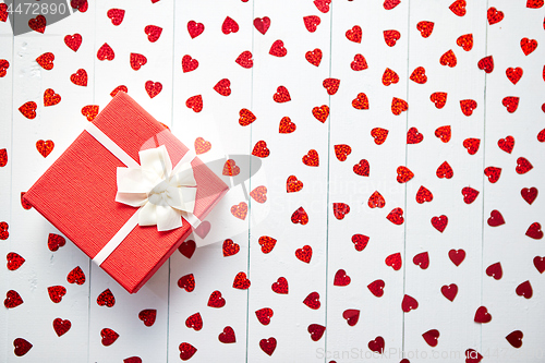 Image of Boxed gift placed on heart shaped red sequins on white wooden table