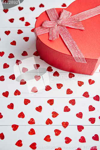 Image of Boxed gift placed on heart shaped red sequins on white wooden table