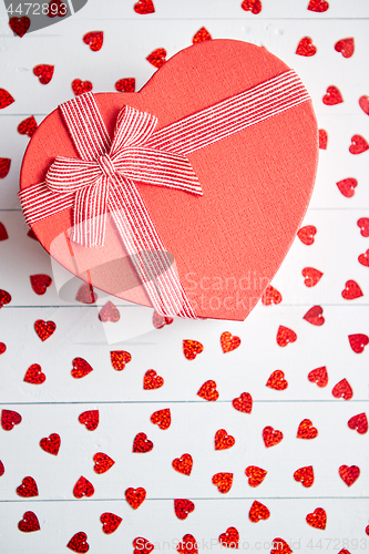 Image of Boxed gift placed on heart shaped red sequins on white wooden table