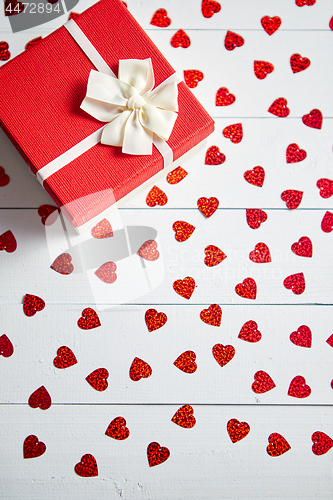 Image of Boxed gift placed on heart shaped red sequins on white wooden table