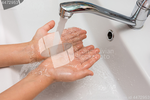 Image of Children\'s hands under a strong stream of water from the mixer in the bathroom