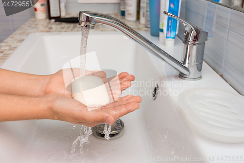 Image of The child holds in his hands the soap on which water flows from the mixer