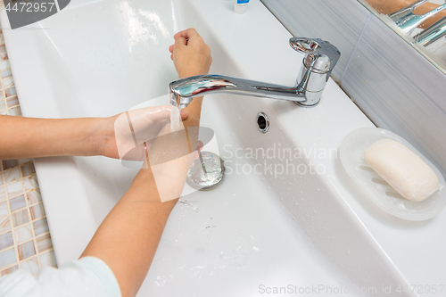 Image of The child washes his hands up to the elbows in the bathroom sink