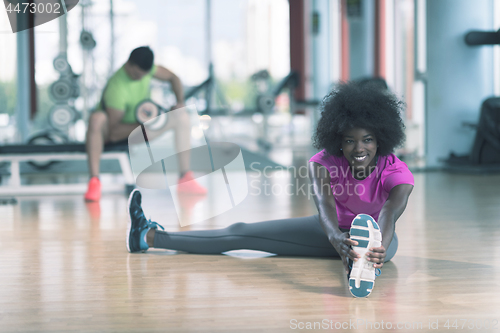 Image of woman in a gym stretching and warming up man in background worki