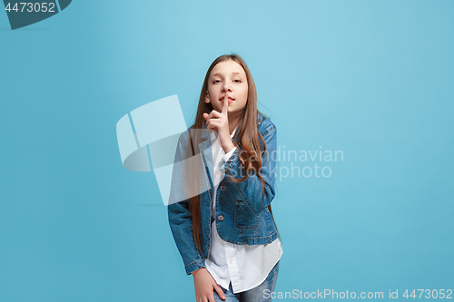 Image of The young teen girl whispering a secret behind her hand over blue background