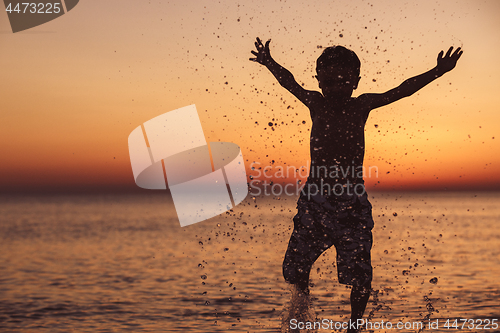 Image of One happy little boy playing on the beach at the sunset time.