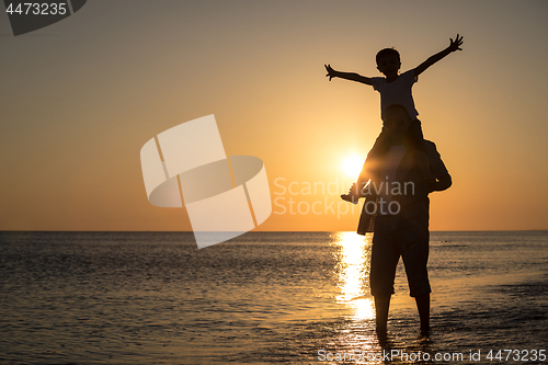 Image of Father and son playing on the beach at the sunset time.