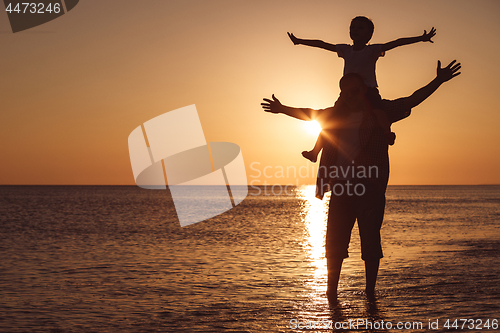 Image of Father and son playing on the beach at the sunset time.