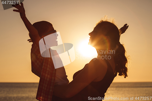 Image of Mother and son playing on the beach at the sunset time.