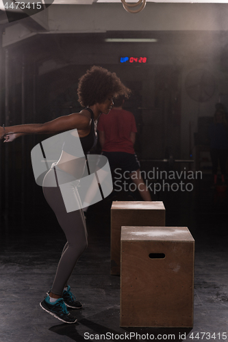 Image of black female athlete is performing box jumps at gym