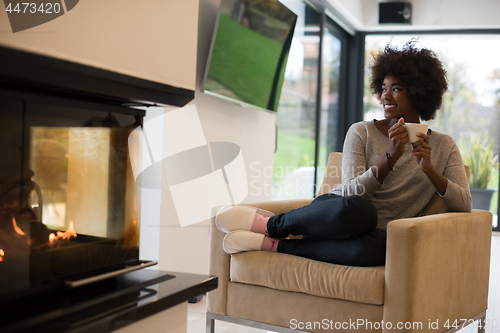 Image of black woman drinking coffee in front of fireplace