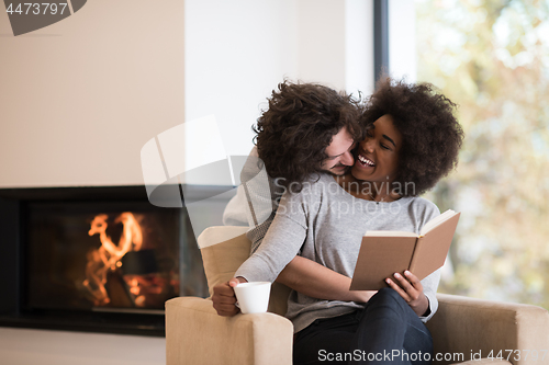 Image of multiethnic couple hugging in front of fireplace