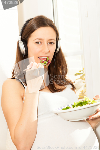 Image of pregnant woman eat salad and listening to music