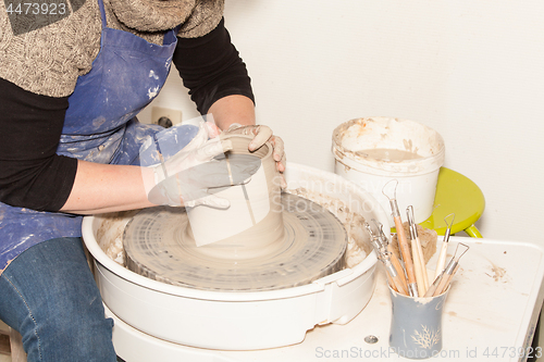 Image of Female Potter creating a earthen jar on a Potter\'s wheel