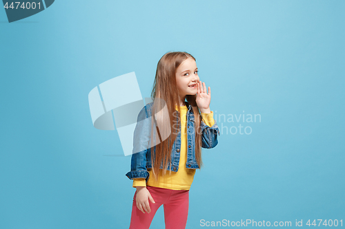 Image of The young teen girl whispering a secret behind her hand over blue background