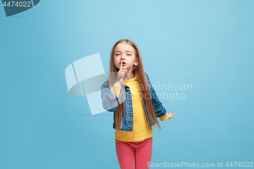 Image of The young teen girl whispering a secret behind her hand over blue background