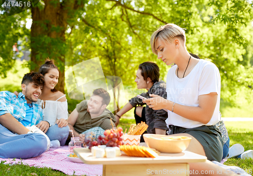 Image of woman using smartphone at picnic with friends