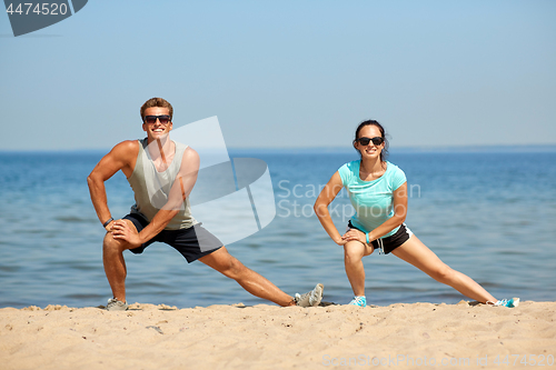 Image of smiling couple stretching legs on beach