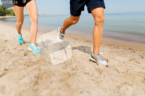 Image of legs of sportsmen in sneakers running along beach