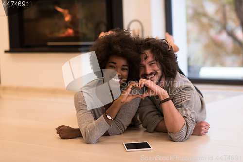 Image of multiethnic couple showing a heart with their hands on the floor