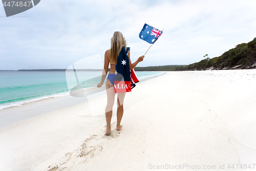 Image of Woman walking along idyllic beach with Australian flag