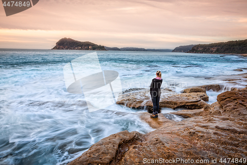Image of Female standing on rocks letting coastal waves wash up to her feet