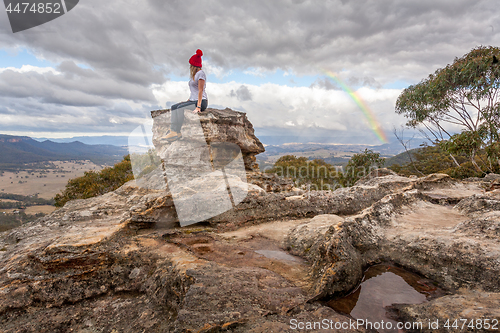 Image of Woman perched on rock pillar peak with the best views below braving the mountain chill