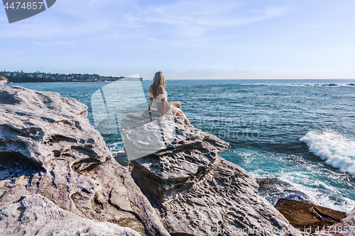Image of Female relaxes perched on a rock enjoying coastal views