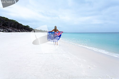 Image of Aussie girl walking along pristine beach with Australian flag