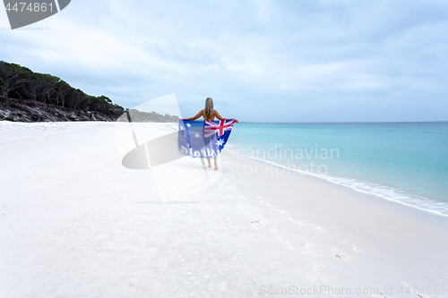 Image of Aussie girl walking along pristine beach with Australian flag